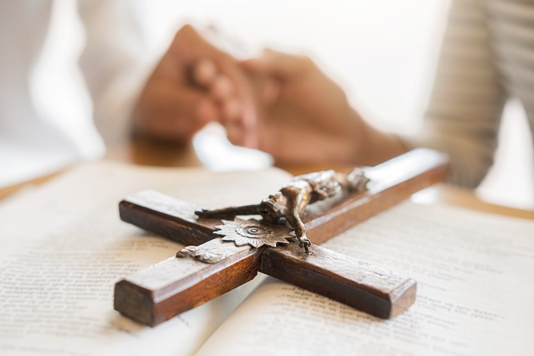 Christian woman praying with hands together on holy bible and wo